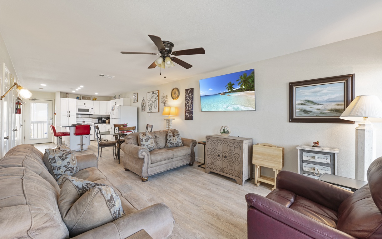 Relax in your spacious living area with plush seating, tropical artwork, and an open kitchen perfect for family meals.