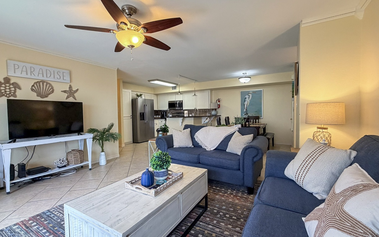 Your spacious living area features comfortable blue sofas, ceiling fan, and open kitchen—perfect for relaxing after beach days.