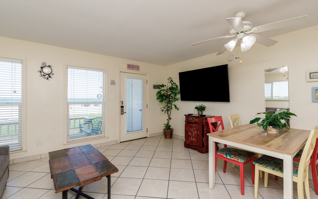 Your bright living space features colorful dining chairs, a ceiling fan for comfort, and a large TV for relaxation after exploring.
