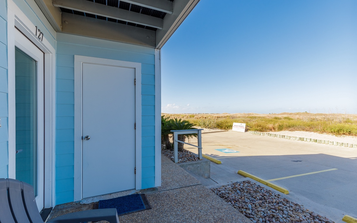 Beach cottage entrance with designated parking and coastal views beyond the dunes.
