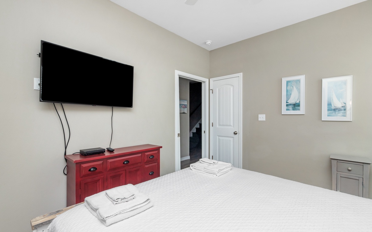 Unwind in your peaceful bedroom with a large flat-screen TV and charming nautical artwork creating a cozy coastal retreat.
