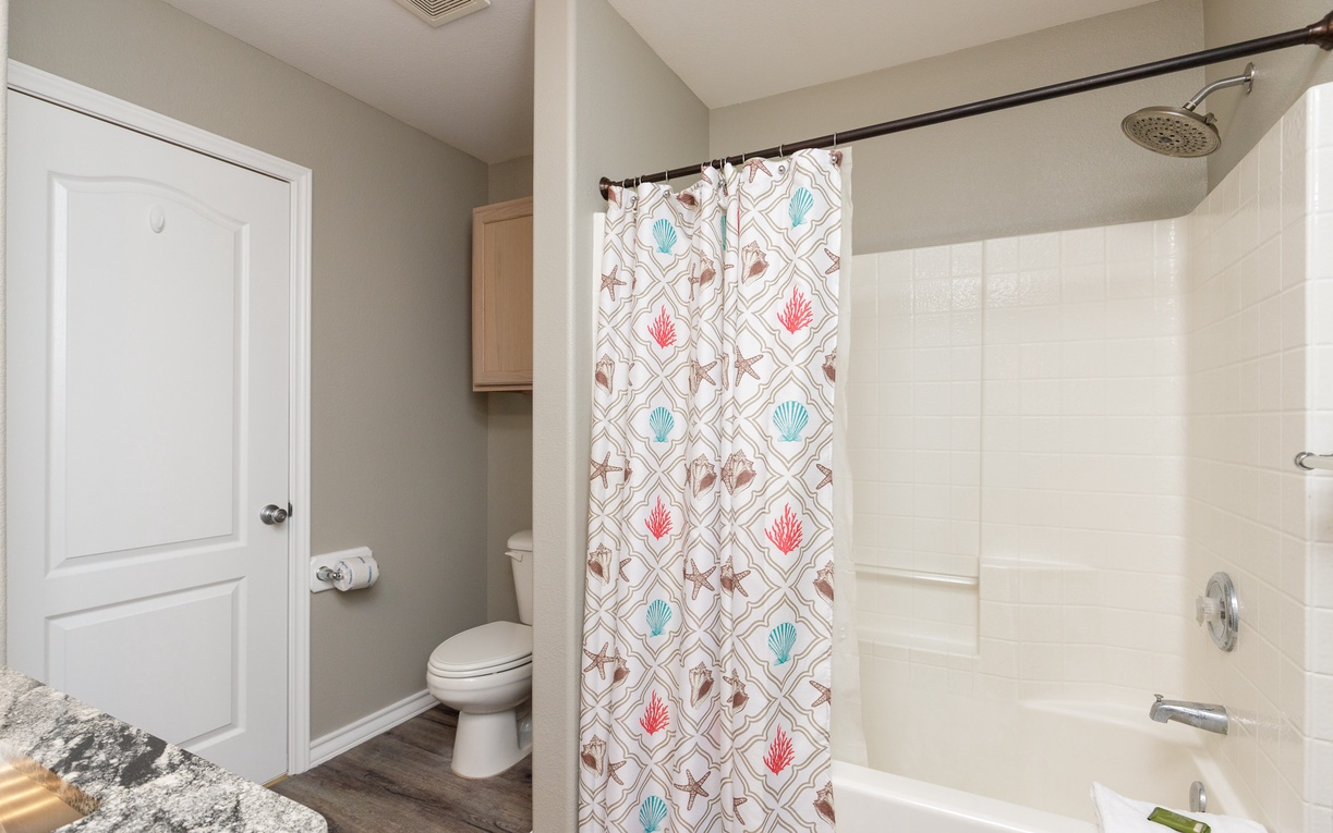 Your private bathroom features a relaxing tub-shower combo with coastal-themed curtain, modern fixtures, and ample storage space.