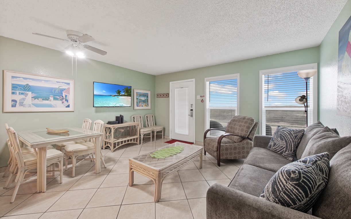 Unwind in your bright, coastal-themed living space with comfortable seating, dining area, and tropical artwork creating the perfect beach getaway atmosphere.