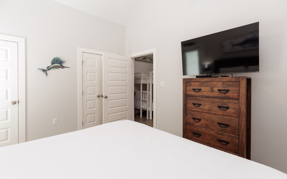 Relax in your peaceful bedroom featuring a plush bed, coastal artwork, flat-screen TV, and warm wood furnishings for ultimate comfort.