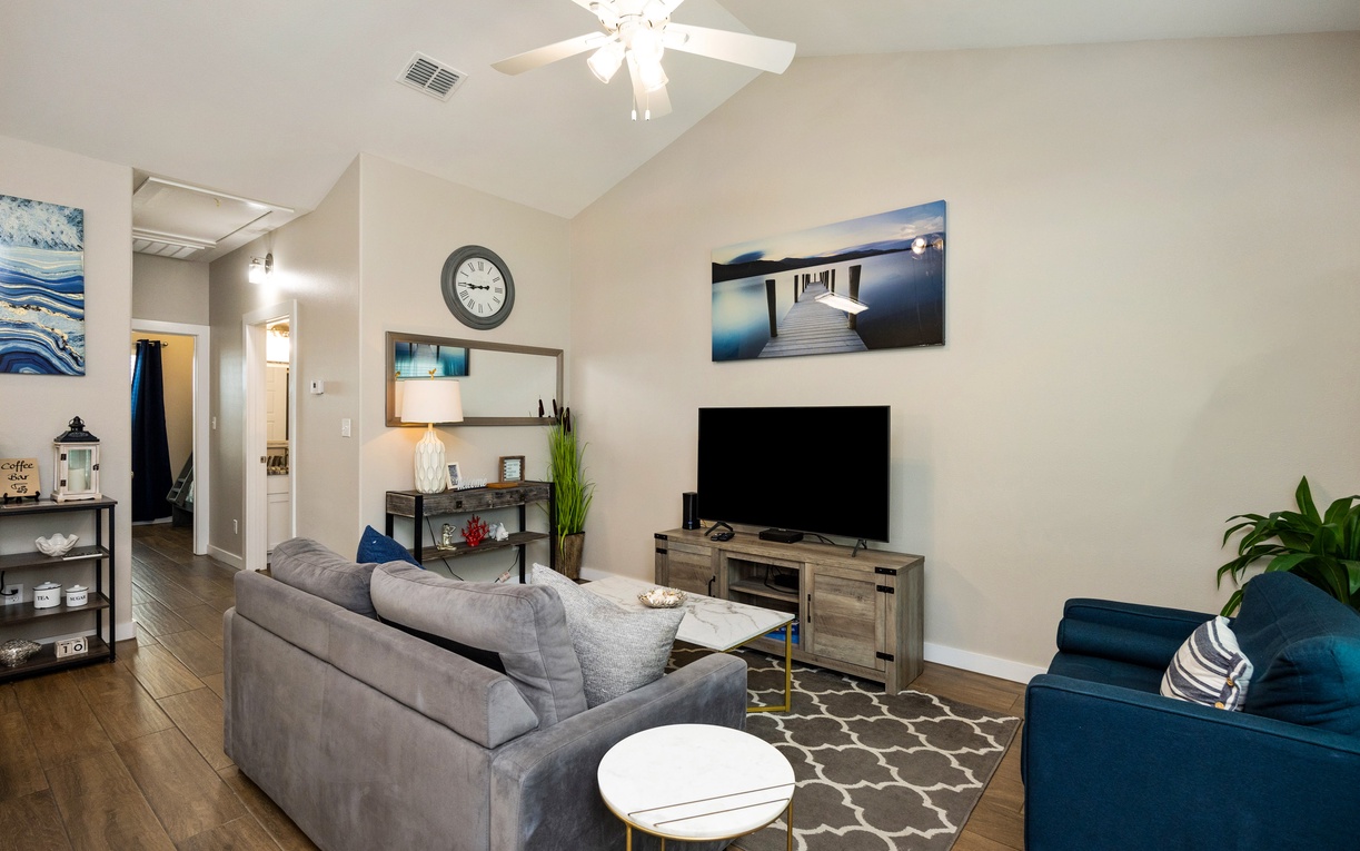 Unwind in your spacious living room with plush seating, modern entertainment center, and calming coastal artwork creating the perfect retreat.