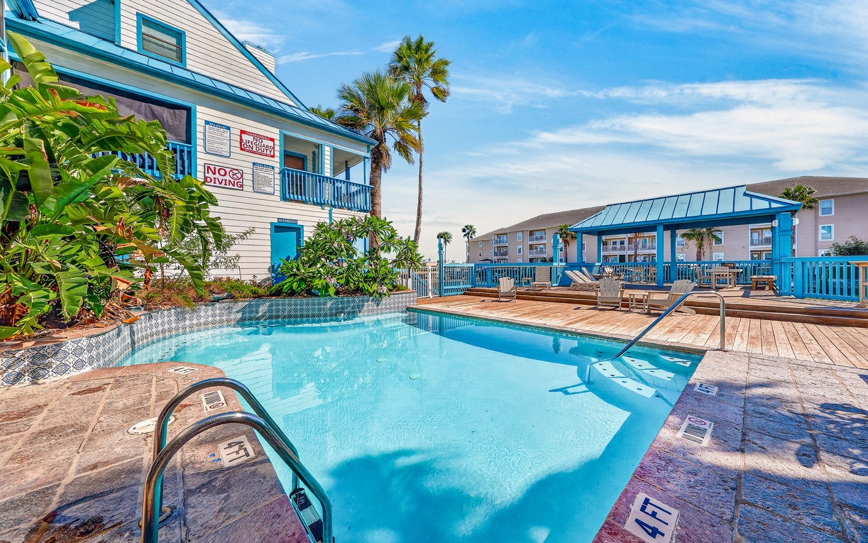 A bright coastal-inspired pool area with vibrant blue accents and tropical palms creates an inviting seaside escape under clear blue skies.