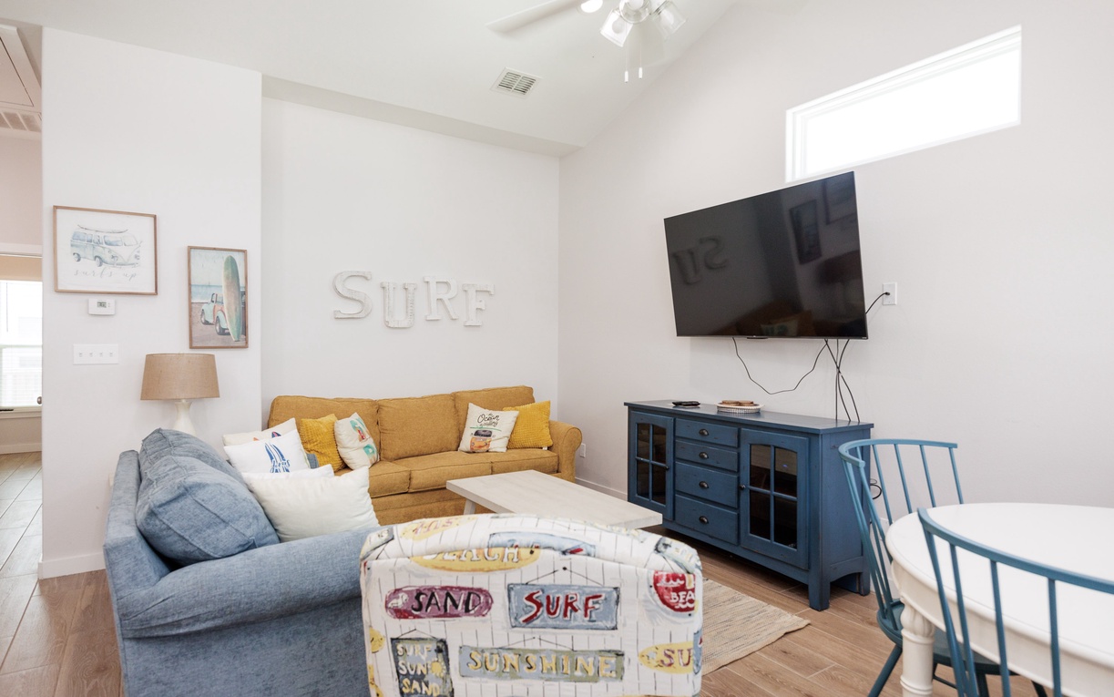 Unwind in your bright, coastal-themed living room with comfortable seating and entertainment setup perfect for relaxing evenings.