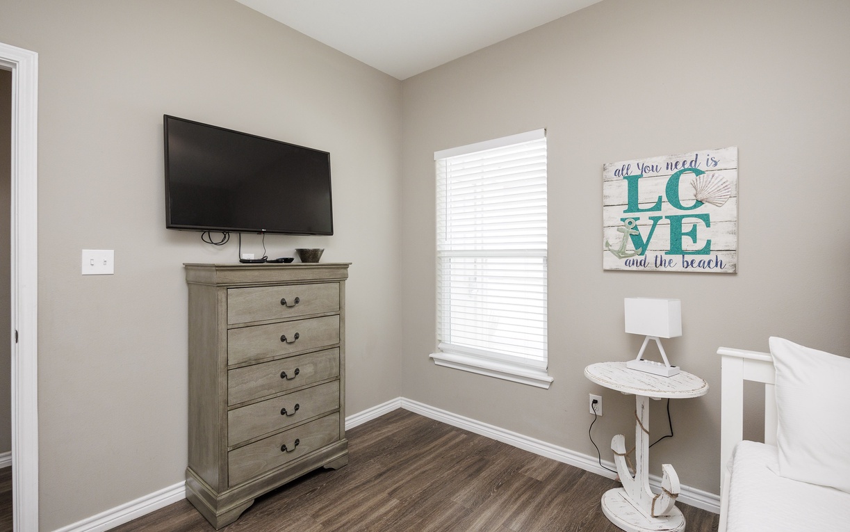 Relax in your peaceful bedroom corner with coastal charm, featuring a flat-screen TV and charming beachy decor.