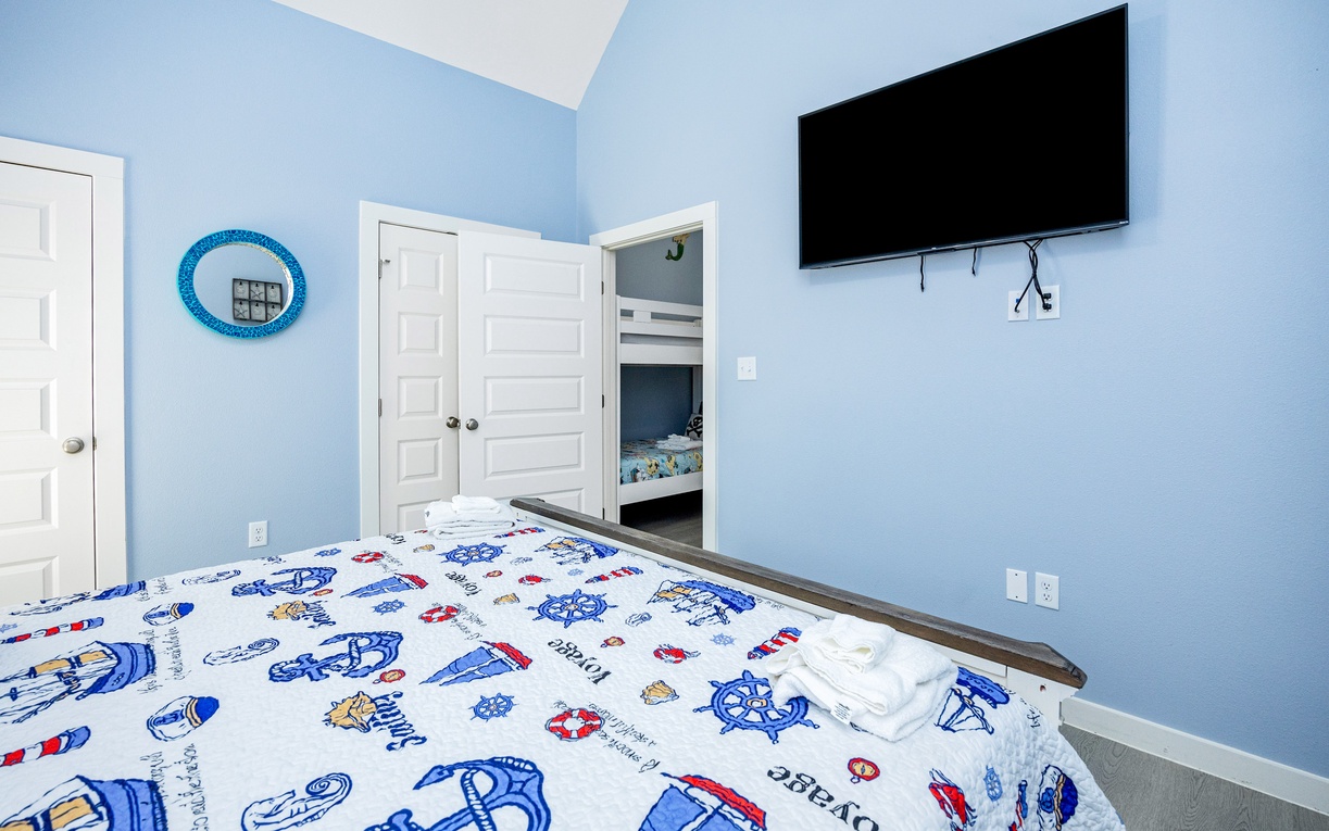 Unwind in your cheerful nautical-themed bedroom featuring calming blue walls, playful maritime bedding, and modern entertainment for cozy nights.