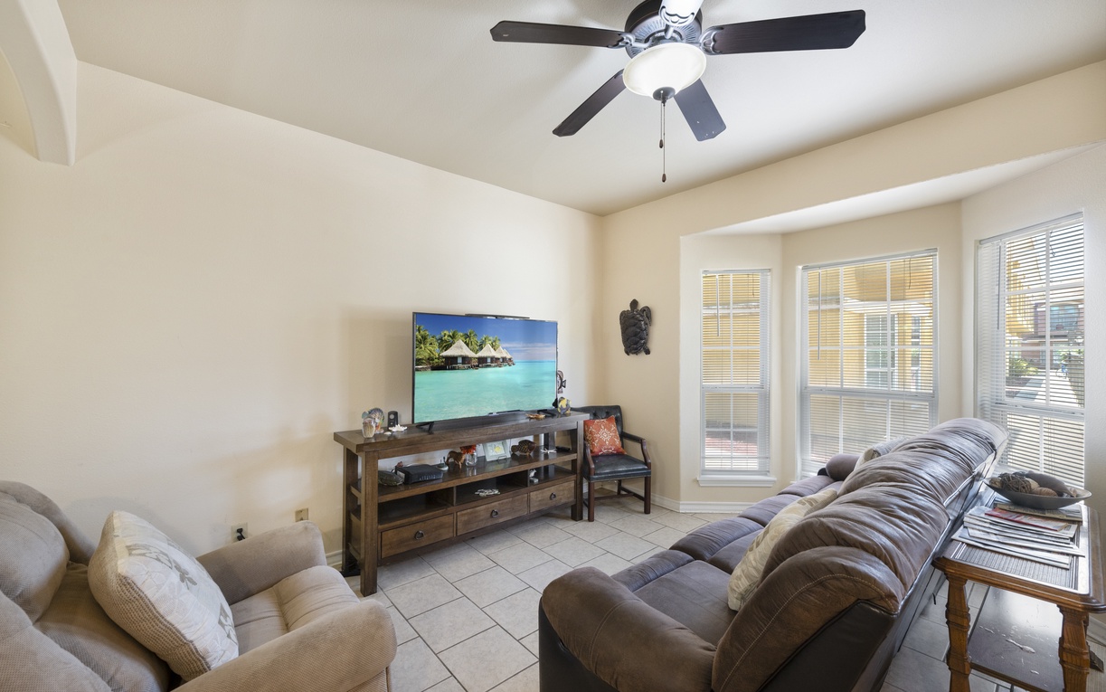 Settle into plush seating, catch your favorite shows on the flat-screen TV, and enjoy the gentle breeze from the ceiling fan. Large windows flood this cozy living room with natural light.