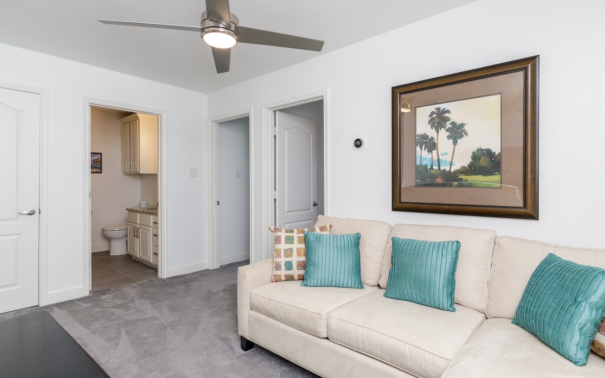 Relax on your plush sofa under the gentle ceiling fan breeze while tropical artwork sets a serene mood in this bright living space.