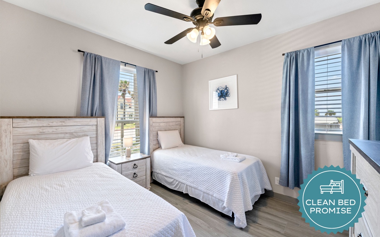 Your comfortable twin bedroom offers restful nights with crisp linens and natural light streaming through blue curtains.