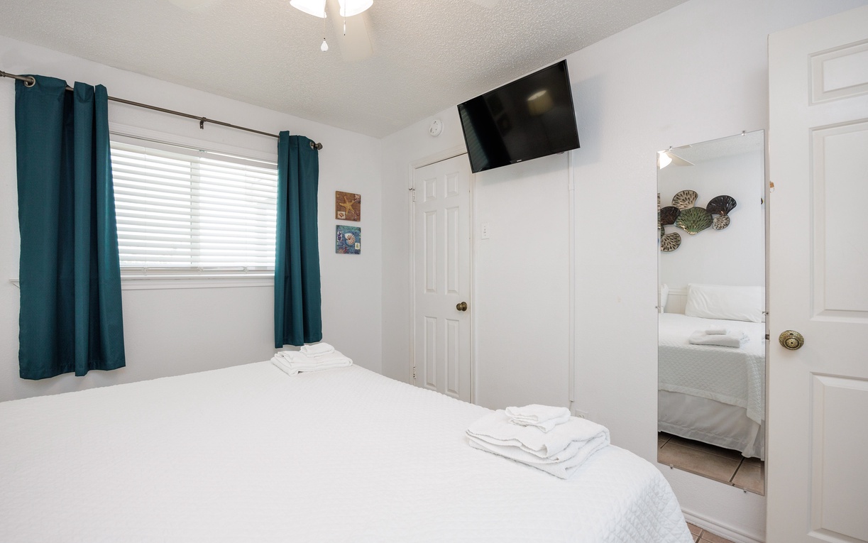Your bright bedroom features crisp white linens, teal accents, and a wall-mounted TV for relaxing evenings after exploring the area.