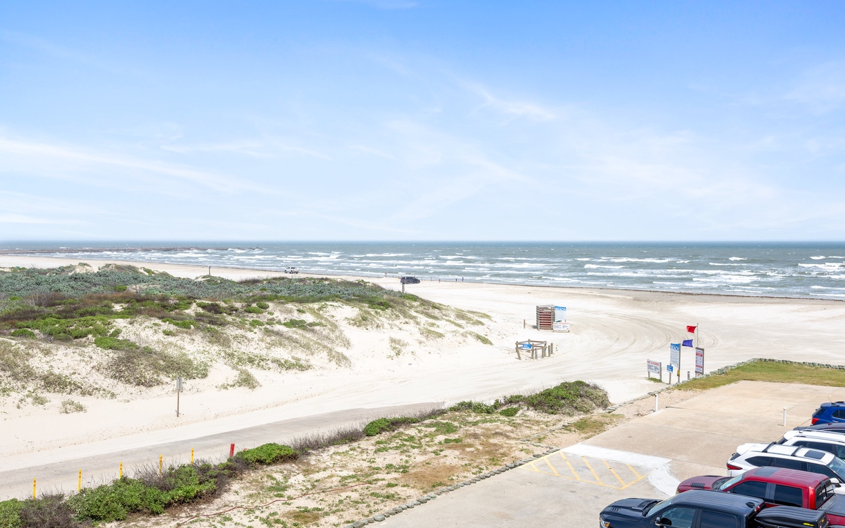 Expansive sandy beach stretches along the coastline with rolling waves and natural dune vegetation creating a pristine coastal setting.