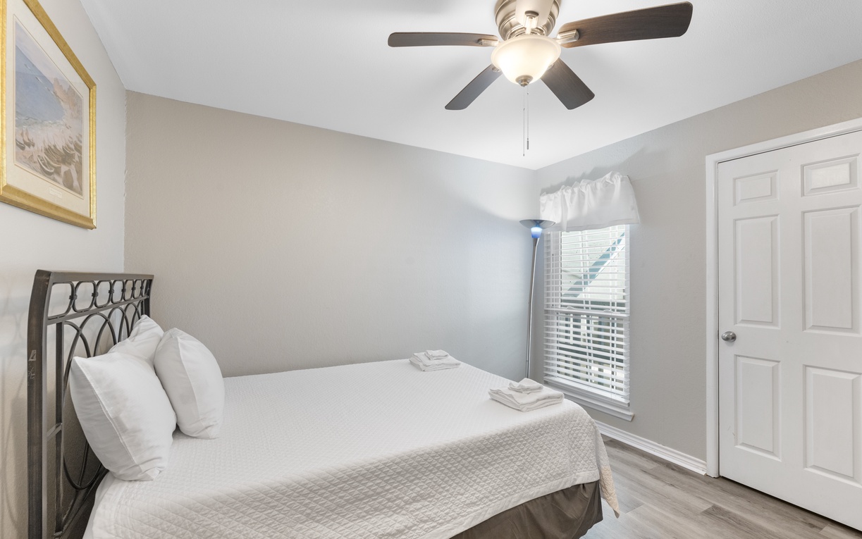 Sink into crisp white linens in your peaceful bedroom, where soft natural light and gentle ceiling fan create the perfect retreat.
