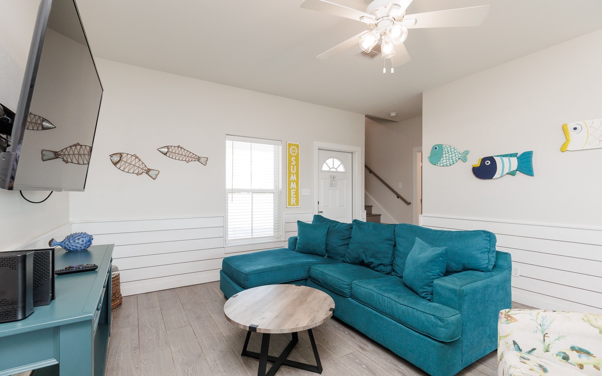 Sink into your comfortable turquoise sectional and unwind in this bright coastal living space, complete with whimsical fish art and a ceiling fan for comfort.