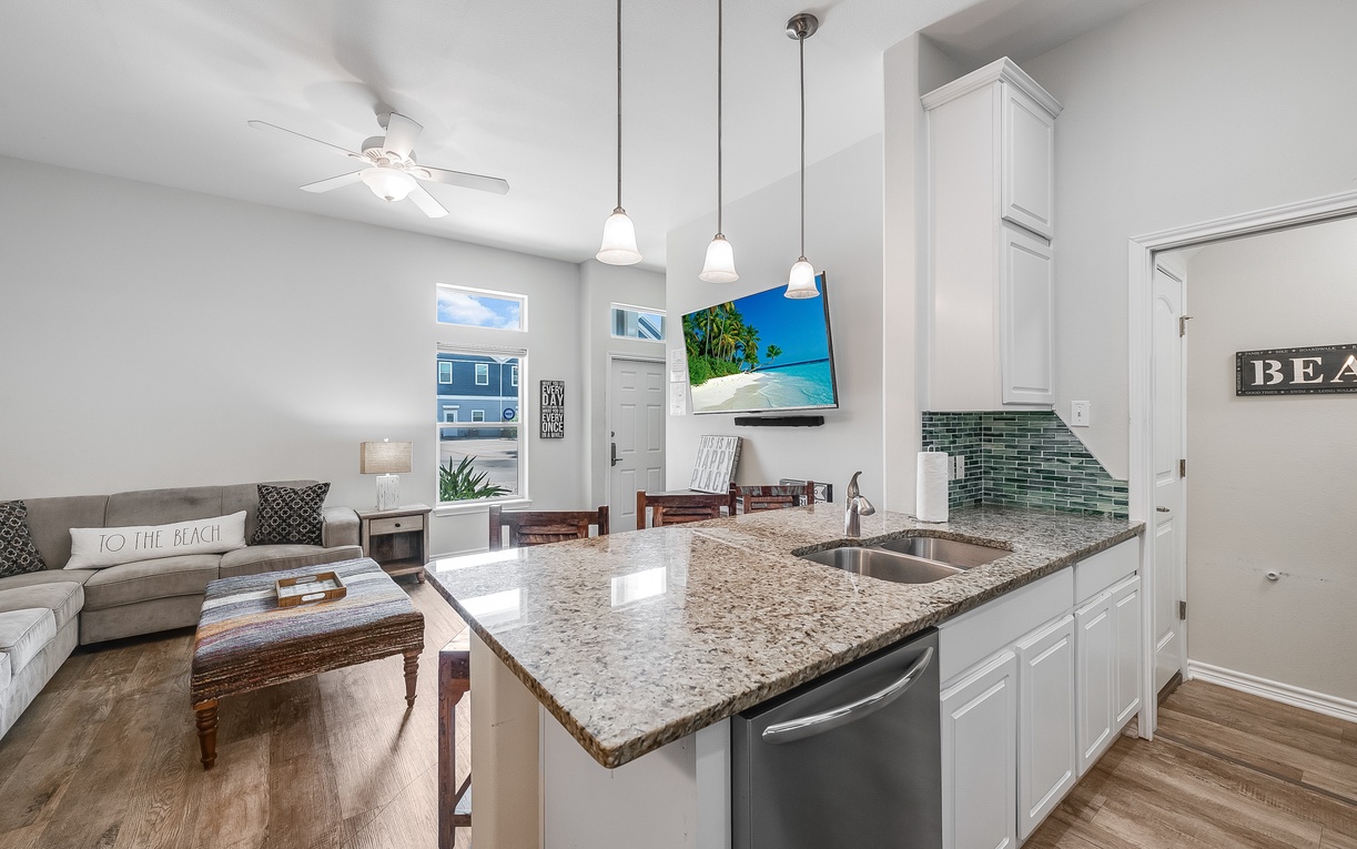 Your modern kitchen island flows seamlessly into the cozy living space, where granite counters and beach-themed touches create the perfect coastal getaway atmosphere.