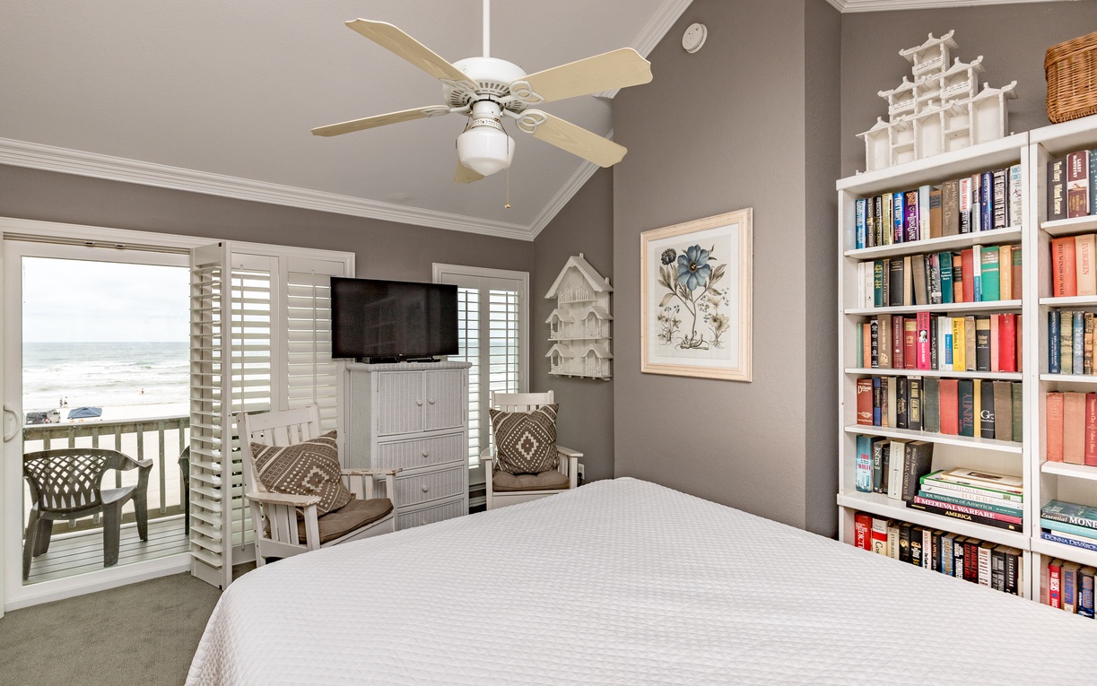 Your peaceful bedroom retreat features a well-stocked bookshelf for evening reads and balcony doors opening to refreshing coastal breezes.