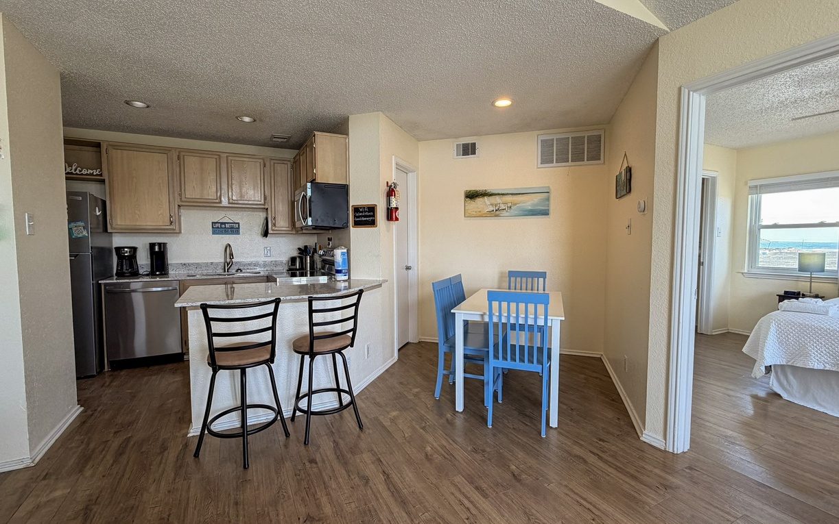Your open-concept living space seamlessly blends kitchen, dining, and relaxation areas with cheerful blue dining chairs and ocean views.