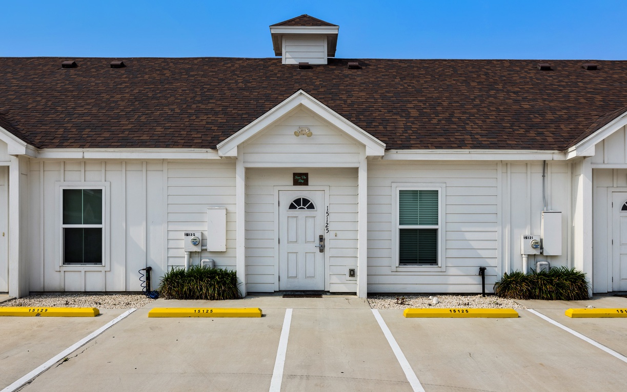 Single-story vacation rental building featuring traditional white siding, dark shingled roof, and dedicated parking spaces for convenient arrival.
