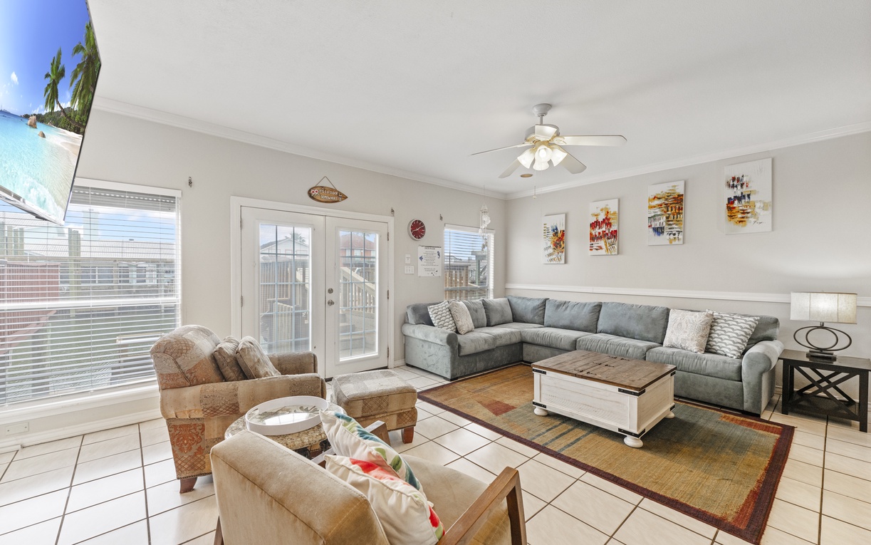 Relax in your spacious living room with plush sectional seating, natural light streaming through French doors, and cheerful artwork adorning the walls.