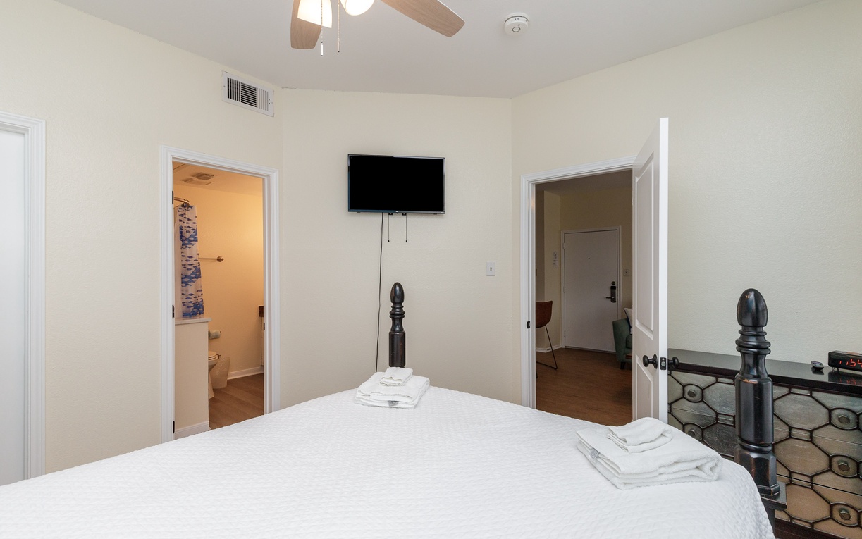 Your serene bedroom features crisp white linens on a queen size bed and a wall-mounted TV for cozy evenings in.