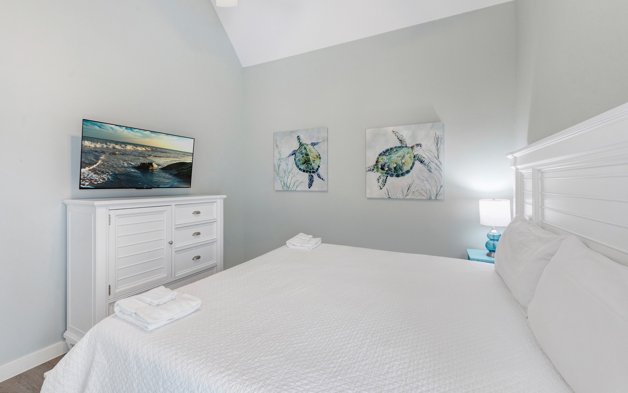 Drift off to sleep in this coastal-themed bedroom with ocean artwork, crisp white linens, and peaceful sea turtle art creating your perfect beach retreat.