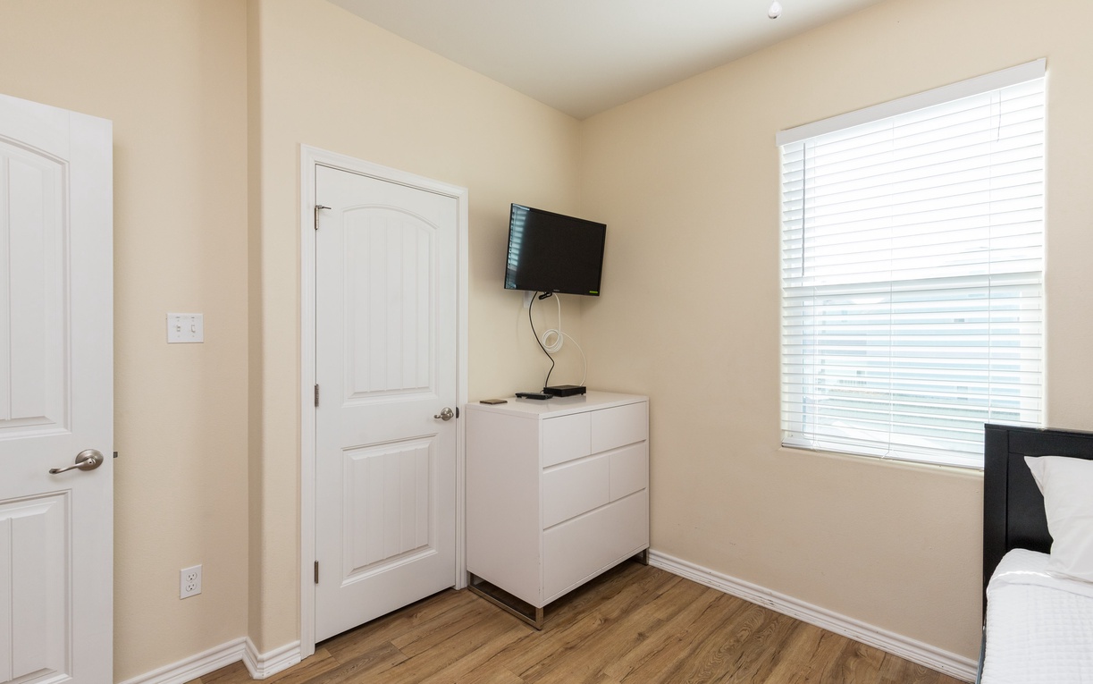 Unwind in your peaceful bedroom with modern amenities like a wall-mounted TV and ample storage in the sleek white dresser.
