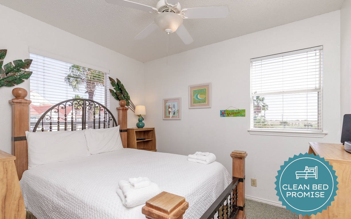 Rest peacefully in your bright bedroom featuring a ceiling fan, artwork, and two windows flooding the space with natural light.