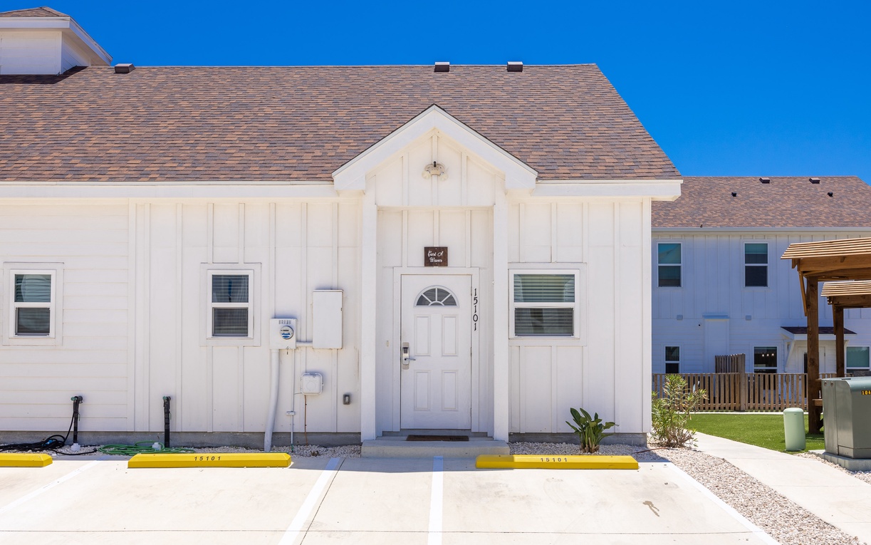 Modern vacation rental with bright white exterior and convenient parking, situated under stunning Texas blue skies.