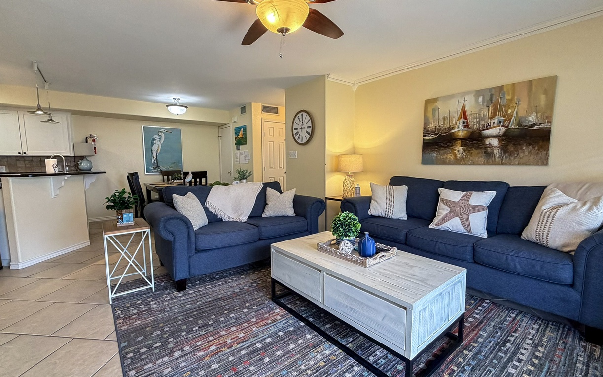 Unwind in your coastal-themed living room with plush navy sofas and open kitchen - perfect for relaxing after beachside adventures.