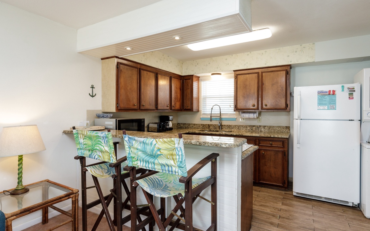 Your fully-equipped kitchen awaits with warm wood cabinets, granite counters, and tropical-themed seating perfect for morning coffee or casual meals.