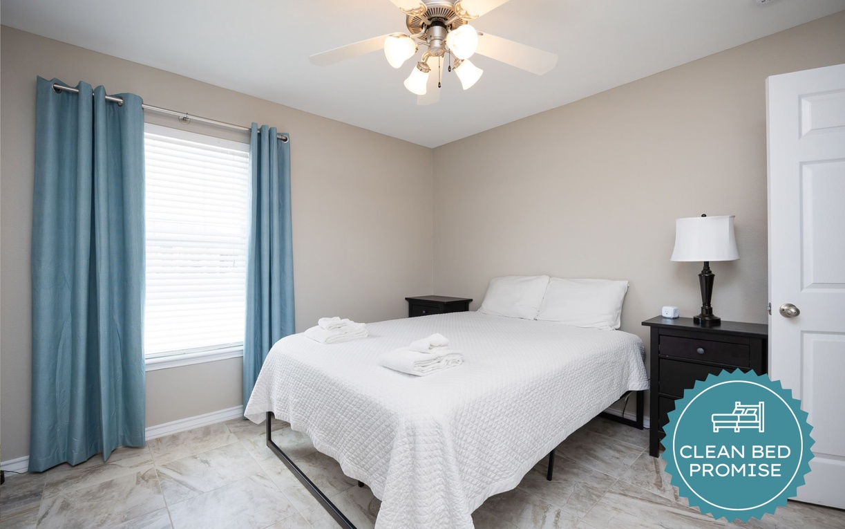 Drift off in your peaceful bedroom with crisp linens, soothing blue curtains, and gentle ceiling fan breezes for perfect sleep.