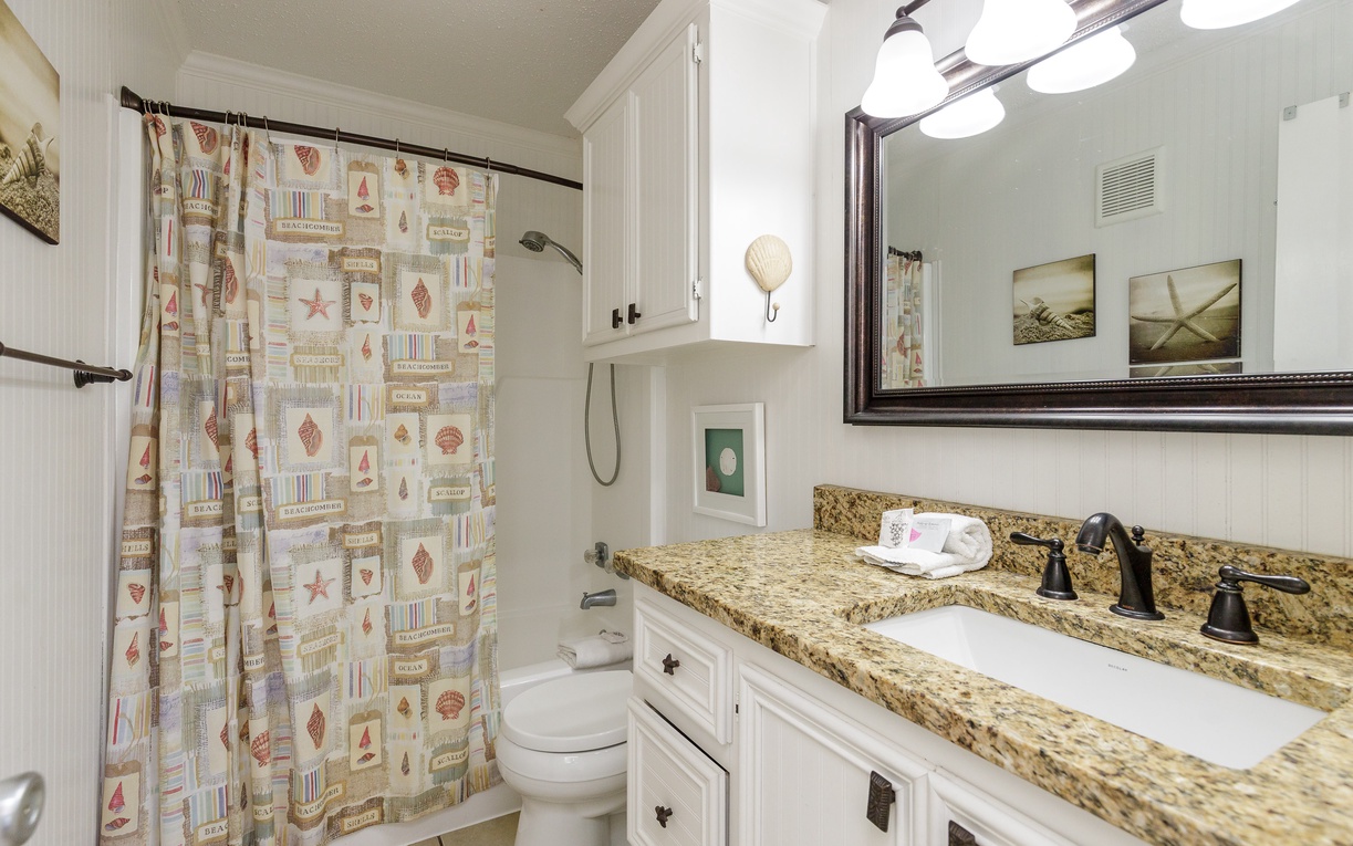 Your bright bathroom features granite counters, white cabinets, and cheerful nautical shower curtains for a fresh, coastal feel.