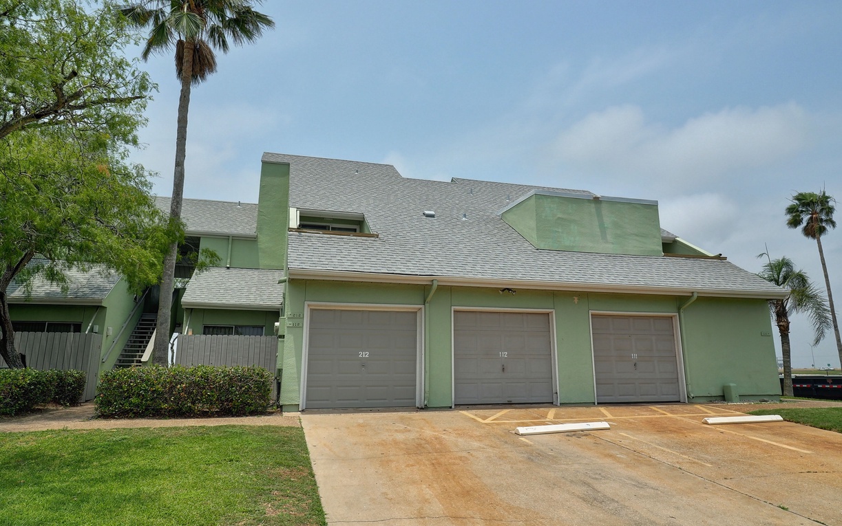Light green property building with three garage spaces and tropical palm trees providing shade in a peaceful residential setting.
