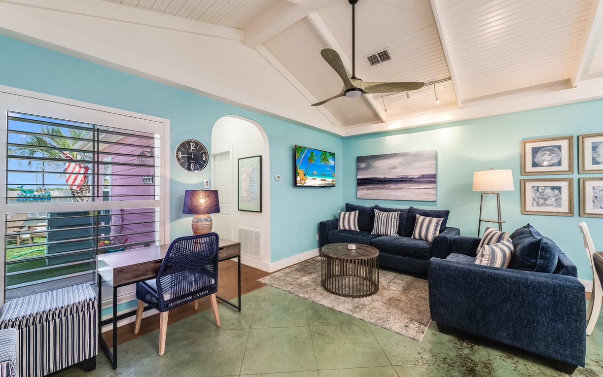Unwind in your coastal living room with soothing turquoise walls, plush navy seating, and tropical artwork creating the perfect beach house vibe.