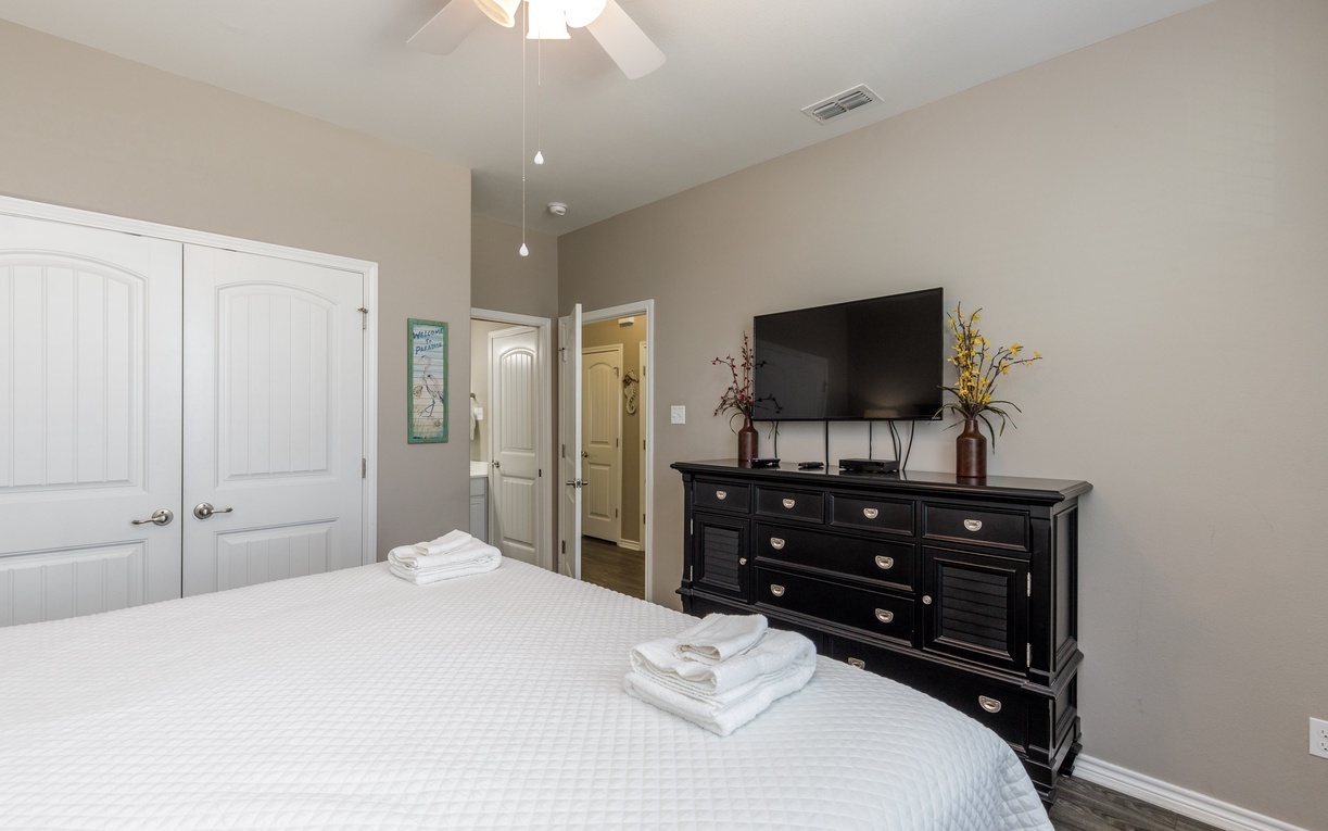 Unwind in your serene bedroom featuring a plush bed, elegant dark wood dresser, and wall-mounted TV for your evening entertainment.