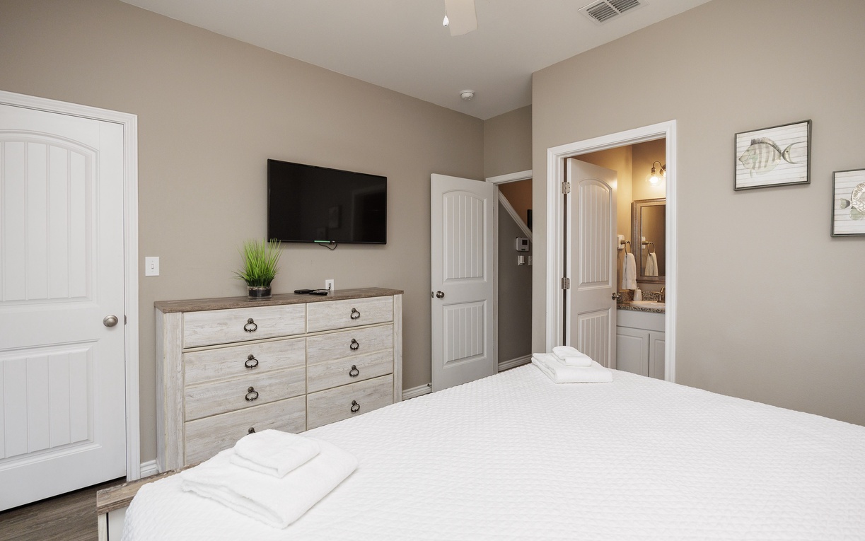 Unwind in your peaceful bedroom featuring a wall-mounted TV, spacious dresser, and ensuite bathroom for ultimate comfort.