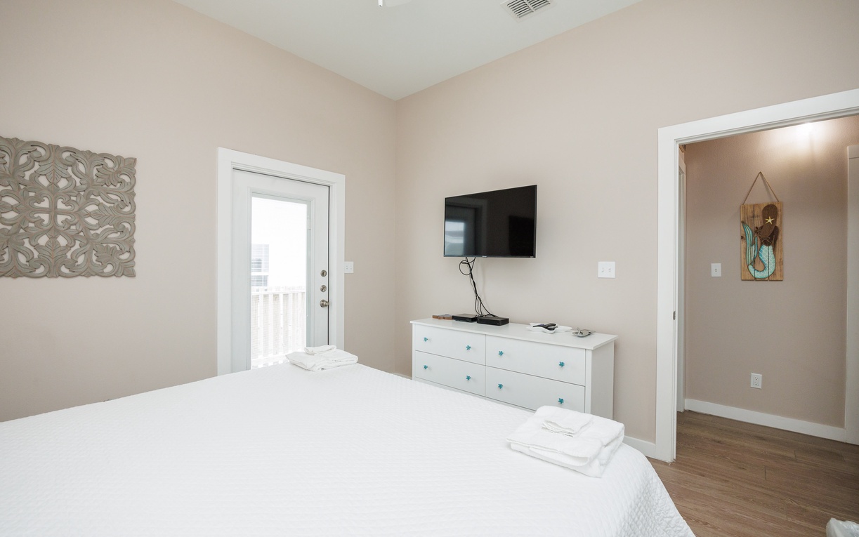 Your peaceful bedroom features crisp white linens and modern amenities, with a mounted TV for entertainment and stylish decor creating a serene retreat.