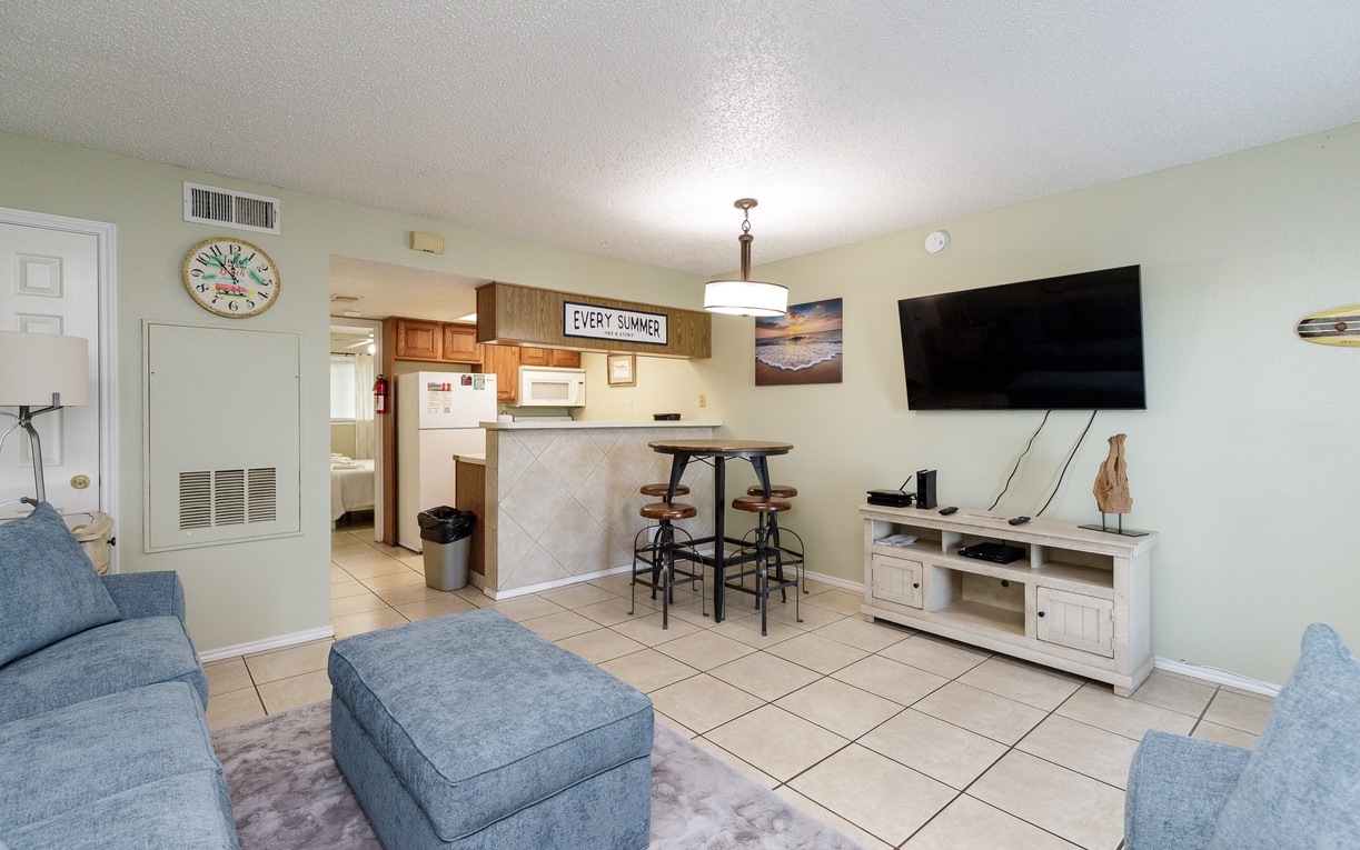 Your cozy living space features comfortable blue seating, a fully equipped kitchen, and entertainment center for perfect vacation relaxation.