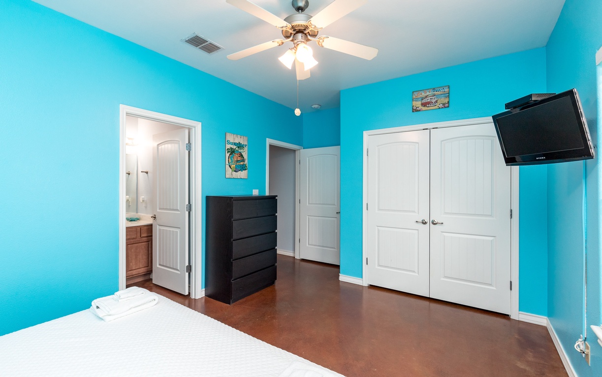 Your bright bedroom features vibrant turquoise walls, cozy ceiling fan, flat-screen TV, and ample storage with built-in wardrobe and dresser.