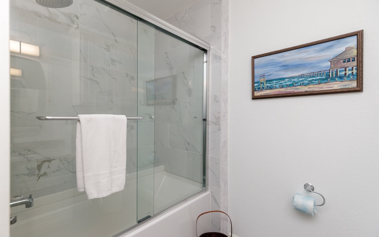 Unwind in your spacious marble shower with rainhead and fresh towels, while coastal artwork creates a serene seaside atmosphere.