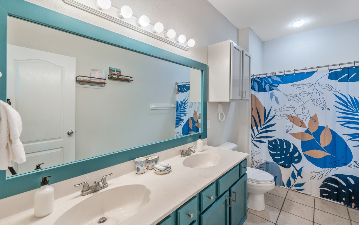 Your bright coastal bathroom features dual sinks and tropical-themed shower curtain, perfect for refreshing after beach adventures.