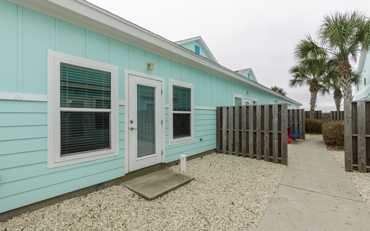 Charming coastal cottage with distinctive turquoise siding and private fenced area surrounded by tropical palms.
