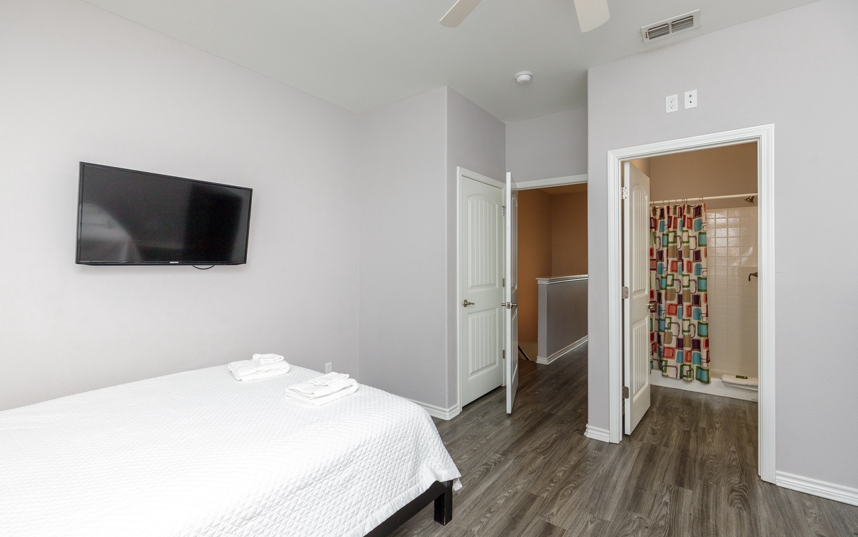 Your contemporary bedroom features crisp linens, a wall-mounted TV for entertainment, and your own private bathroom with colorful shower tile accents.
