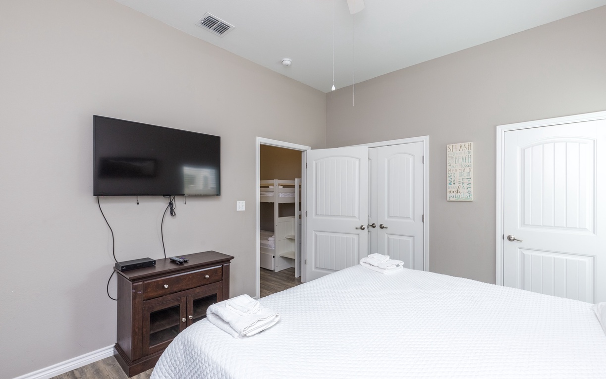 Unwind in your serene bedroom with cozy bedding, entertainment center, and glimpse of bunk beds through the doorway.