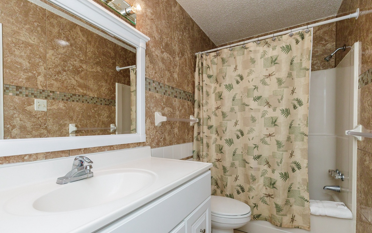 Your private bathroom features a peaceful fern-patterned shower curtain and warm marble tiling that creates a spa-like atmosphere for your morning routine.