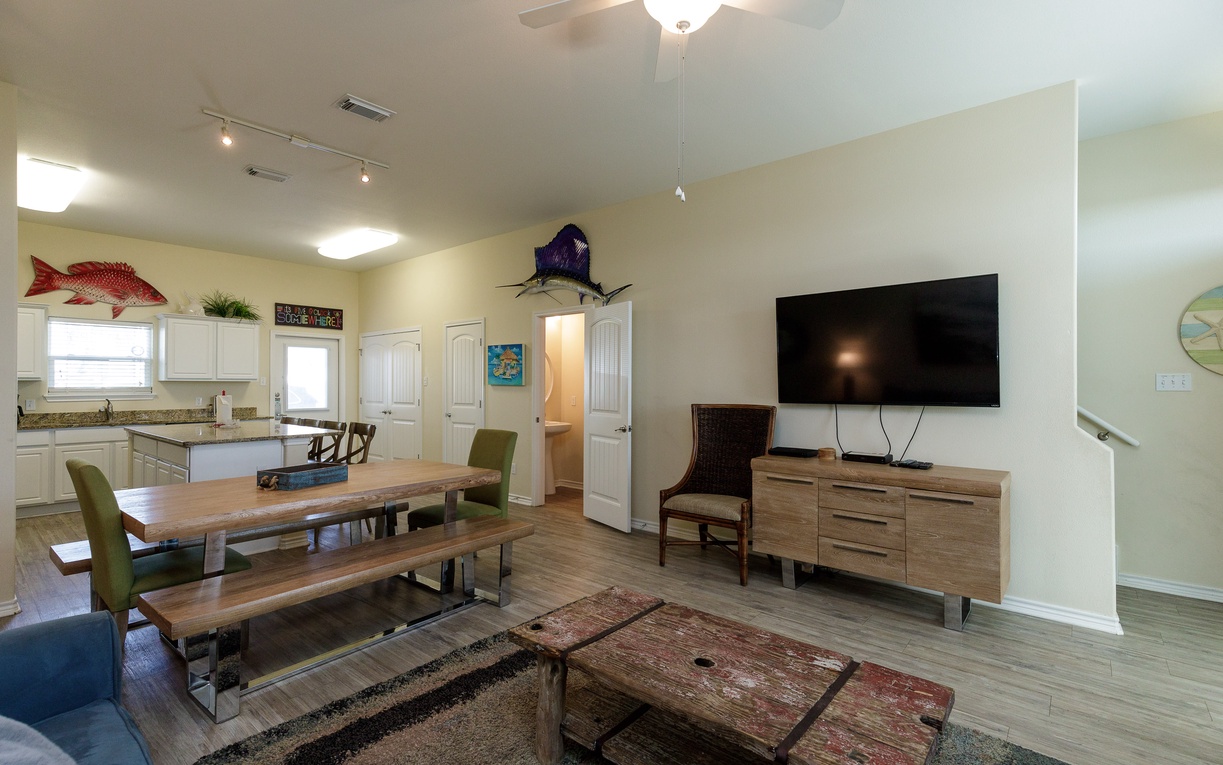 Your open-concept living space combines comfort with coastal charm. Gather around the rustic dining table or relax with entertainment on the large TV.