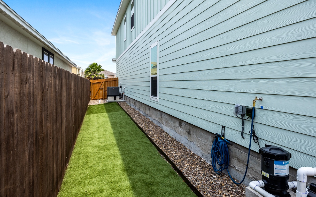 A tidy side yard with artificial turf and modern light blue siding creates a clean, low-maintenance outdoor space perfect for relaxation.