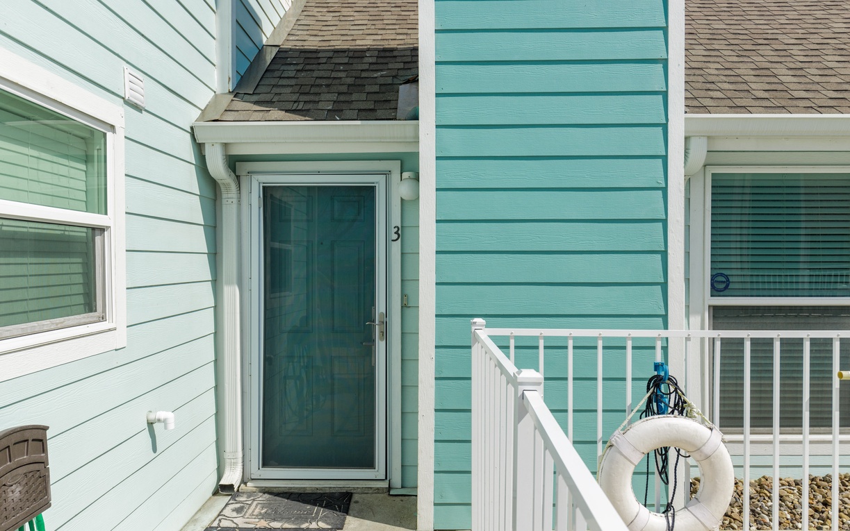 Charming coastal entrance with turquoise siding and white railings creates a welcoming seaside retreat arrival experience.